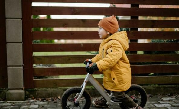 En liten pojke cyklar vid staket.