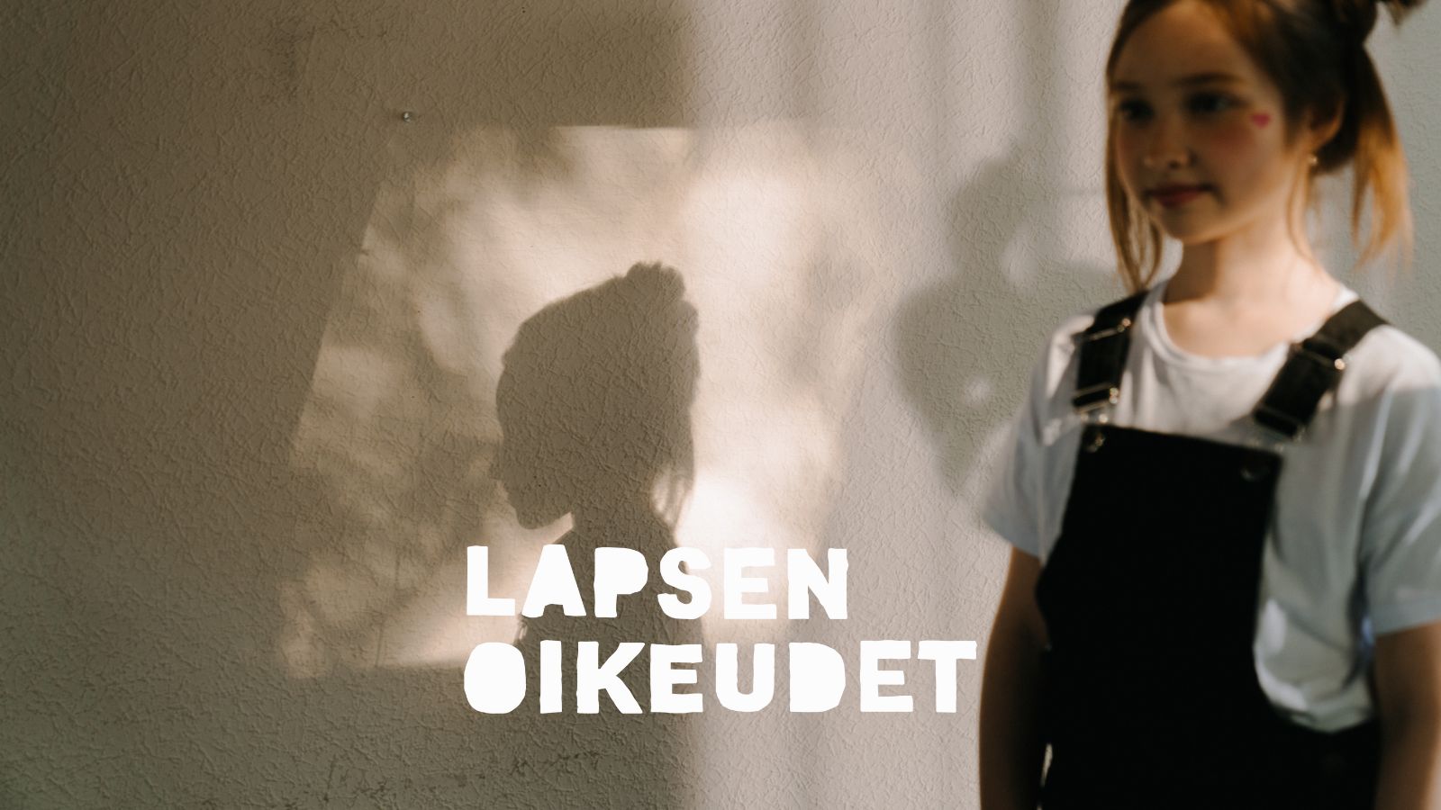 Lapsi etualalla, lapsen varjo heijastuu seinään.
