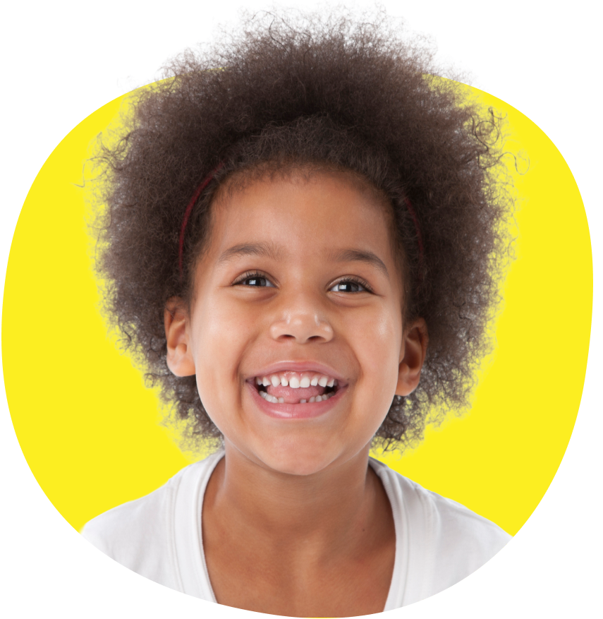 En glad, liten flicka med lockigt hår skrattar mot gul bagrund.