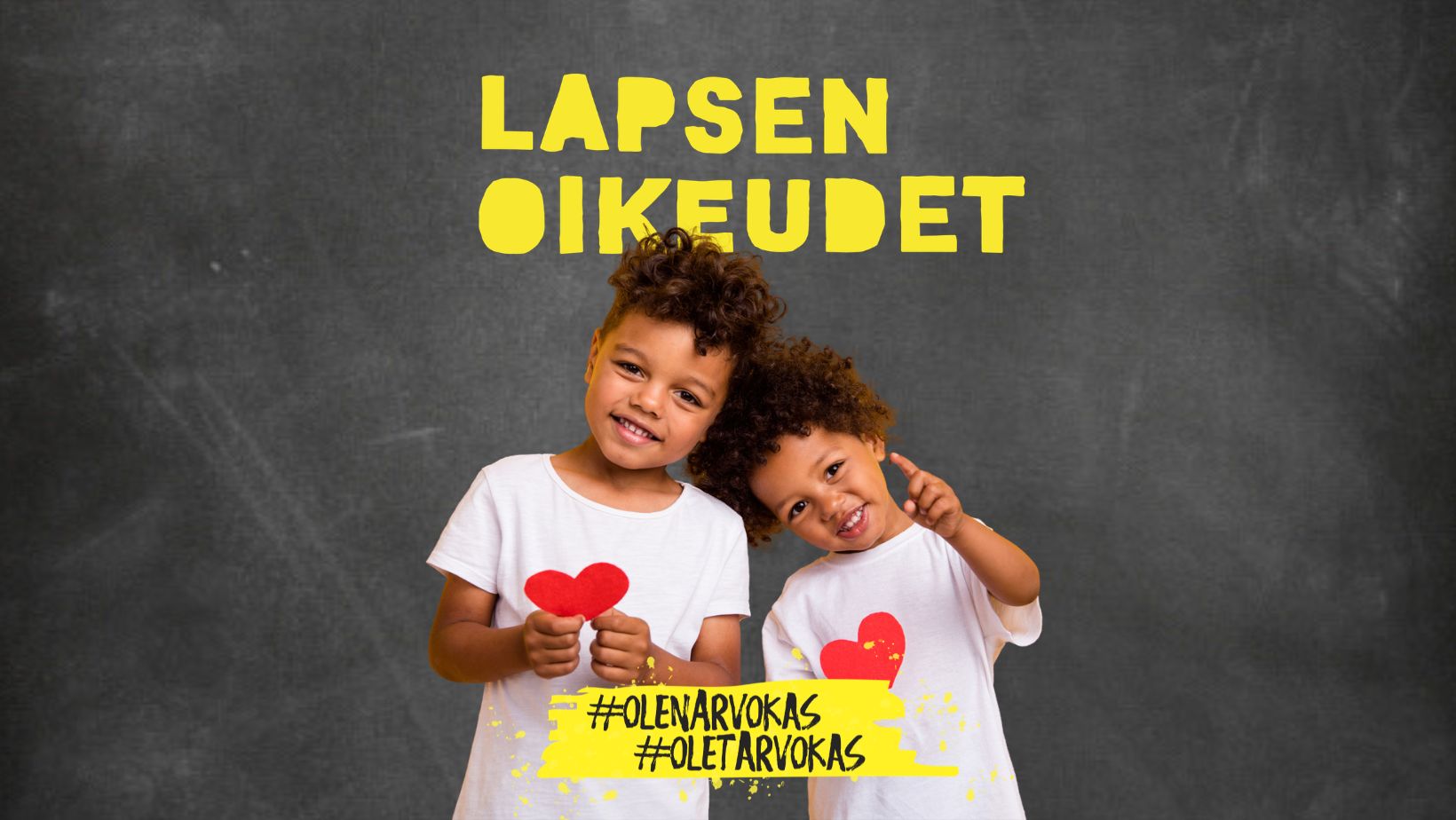 Kaksi lasta pitää paperisydäntä käsissään ja hymyilee.