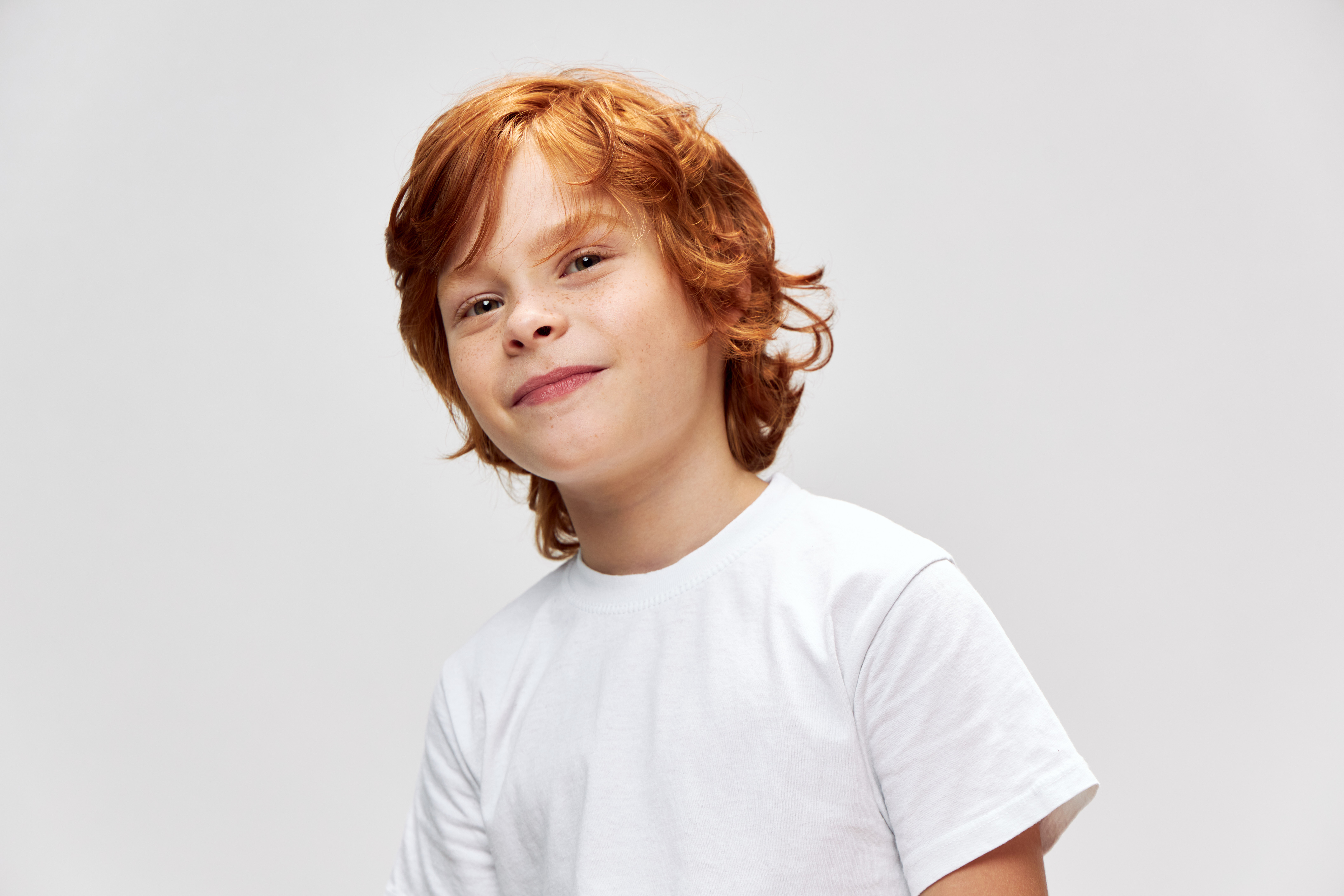 A redheaded boy smiling in front of a grey background.