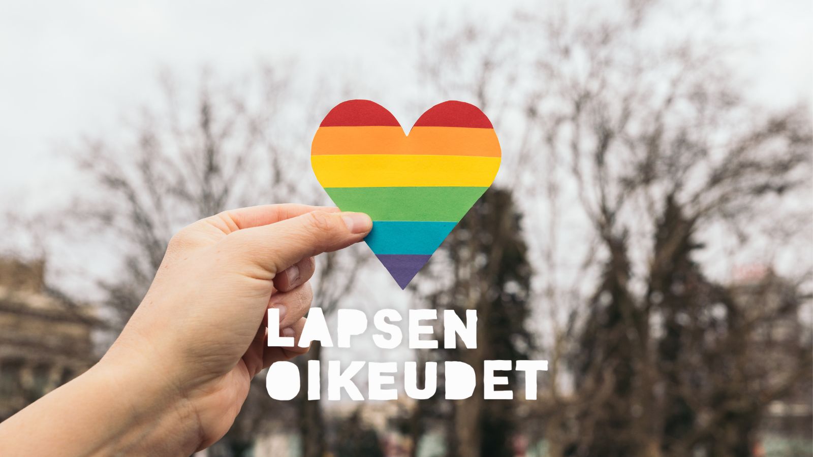 Käsi pitelee sateenkaaren väreissä olevaa sydäntä.
